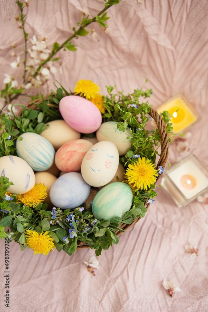On a pastel bedspread is a basket of grass and bright flowers. The basket contains Easter eggs painted with watercolors in beautiful pastel colors.