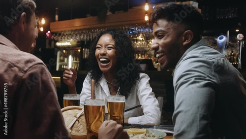 A multiracial woman having dinner and beers with a group of friends at a restaurant and laughing at something her friend said