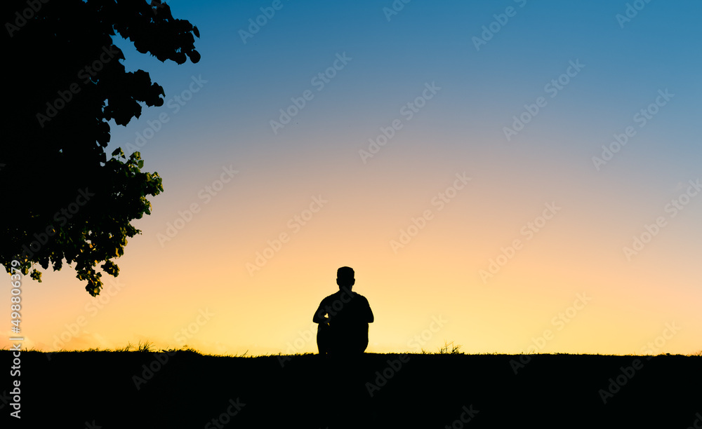 Thoughtful man sitting sitting on a hill facing the sunset 