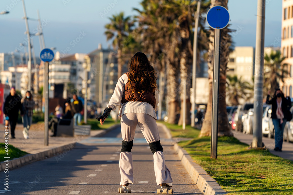 unknown young woman roller skates down the street at sunset in La Serena, back view