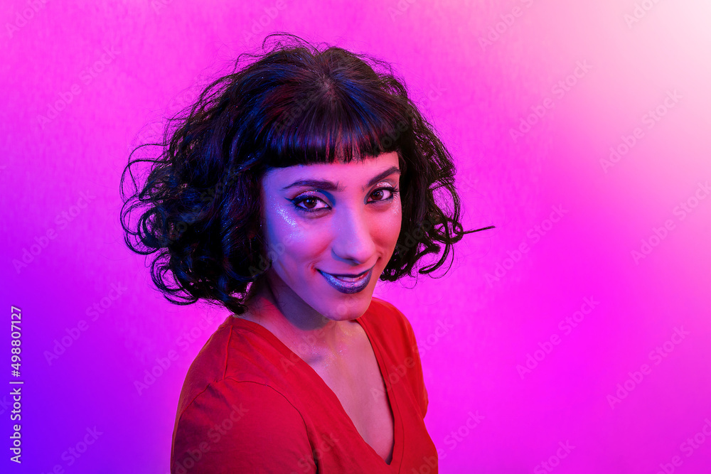 The young woman in the red t-shirt is looking at the camera. Portrait of smiling modern woman with trendy look and bright colors. The young woman in the red t-shirt is looking at the camera. Portrait of smiling modern woman with trendy look and bright colors.