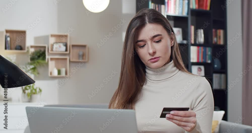 Pretty joyful Caucasian woman sitting at home and shopping online with credit card. Beautiful female buyer paying for purchase by Internet at laptop computer. Shopaholic. Purchasing. Pretty joyful Caucasian woman sitting at home and shopping online with credit card. Beautiful female buyer paying for purchase by Internet at laptop computer. Shopaholic. Purchasing.