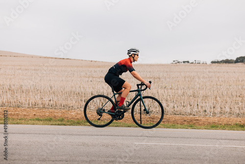 Side view of a female cyclist riding bike against field