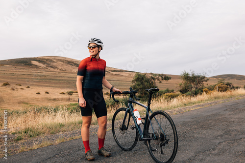 Female cyclist taking break from riding bike standing on empty road