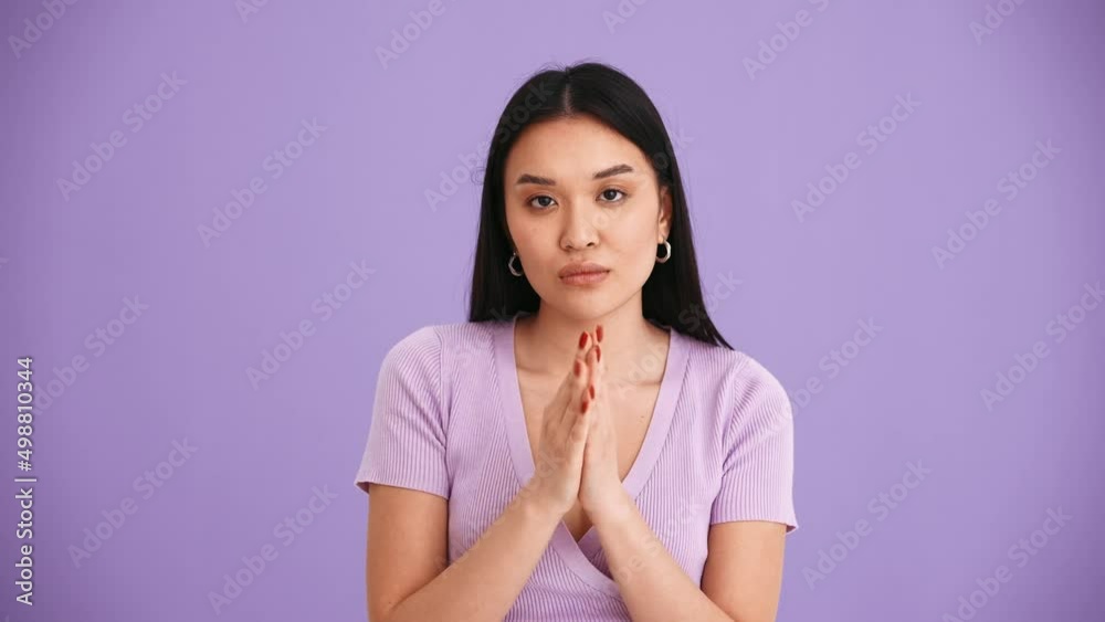 Sad Asian brunette woman wearing purple t-shirt clapping hands at the camera in the purple studio Sad Asian brunette woman wearing purple t-shirt clapping hands at the camera in the purple studio