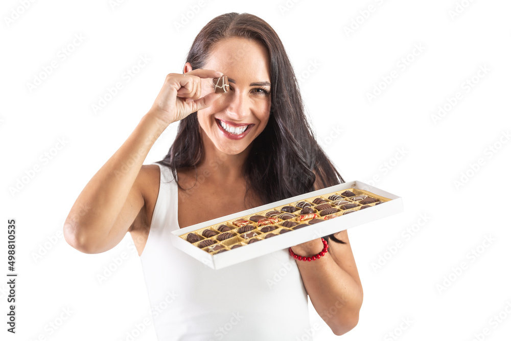 Happy brunette is smiling widely with candy box in her hand and a little chocolate in fron of her eye. Isolated background Happy brunette is smiling widely with candy box in her hand and a little chocolate in fron of her eye. Isolated background