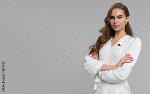 Welcome to our beauty salon. Portrait of mature cosmetologist in white lab coat looking at camera with smile while posing arms crossed at her clinic. Copyspace