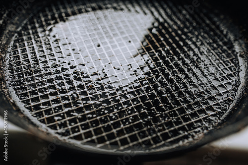 Background, texture, top view of a black frying pan with a checkered pattern, after cooking, smeared with sunflower oil. Photo of dirty dishes. © shchus
