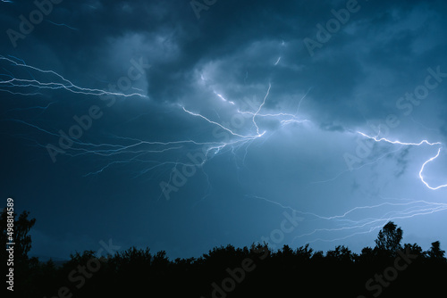 Electrical discharges during a summer storm, branched lightning bolts in the night sky.