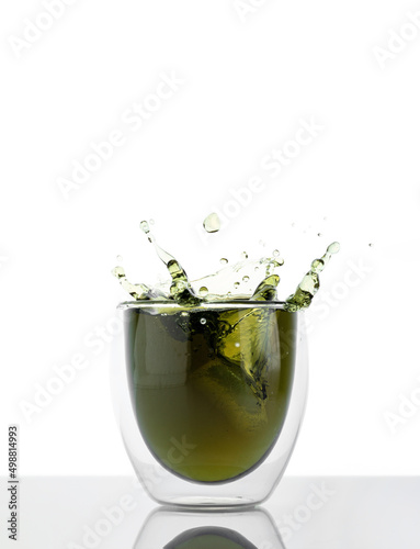 Glass of water with chlorophyll extract against white grey background. Liquid chlorophyll in a glass of water with splash. Concept of superfood, healthy eating, detox and diet, copy space, vertical