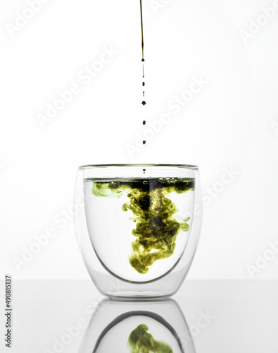 Glass of water with chlorophyll extract against white grey background. Pouring liquid chlorophyll in a glass of water. Concept of superfood, healthy eating, detox and diet. Vertical photo