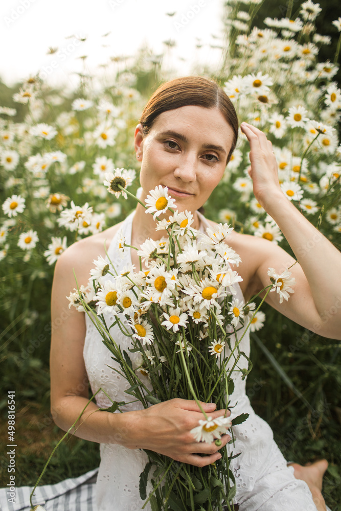 a girl with a big bouquet of daisies sits on the field