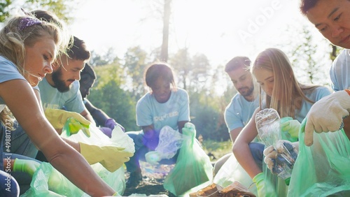 Diverse people eco volunteers in same t shirts taking plastic trash and putting it to bin bag . Group of eco people cleaning public park. Concept of care about nature