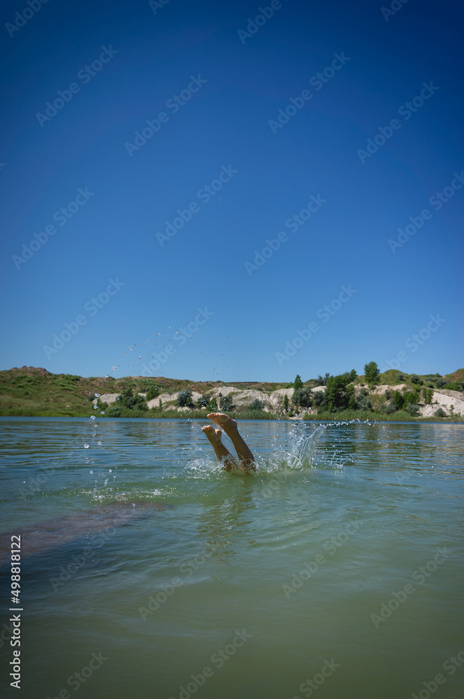 A little cute girl in a swimsuit jumps into the blue water of a career lake.