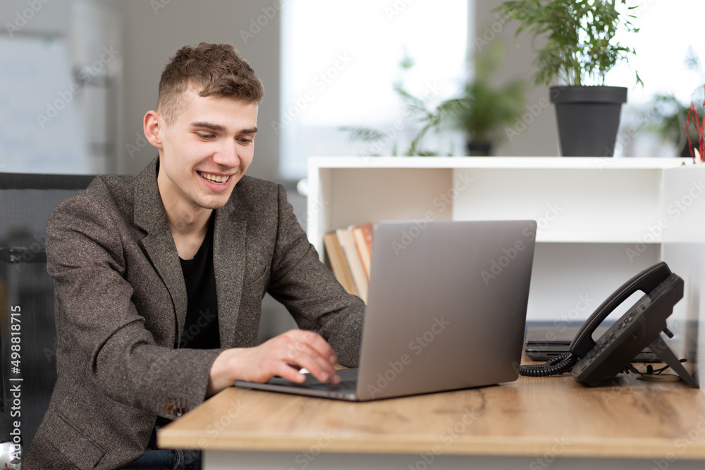 young attractive man sitting in a chair in the office, working on laptop online, smiling, cheerful mood, freelancer, free time, relaxed, modern lifestyle young attractive man sitting in a chair in the office, working on laptop online, smiling, cheerful mood, freelancer, free time, relaxed, modern lifestyle