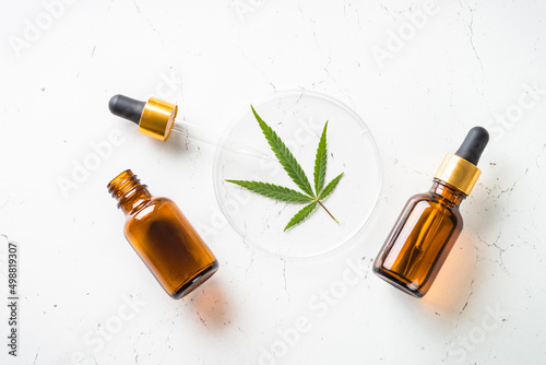 CBD oil, petri dish and cannabis leaves at white table. Medicine and cosmetic product. Flat lay image. photo