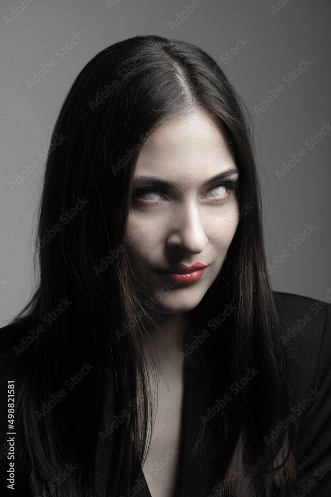 Beauty, make-up, horror and fashion concept. Sexy and beautiful woman with white eyes, red lips and long dark hair looking with uncomfortable and horrifying look. Model wearing black suit