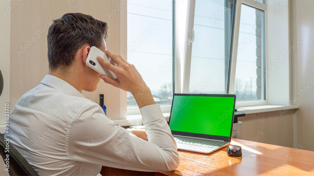 A young man sitting in office talking on the phone in front of a computer with a green screen. High quality photo A young man sitting in office talking on the phone in front of a computer with a green screen. High quality photo