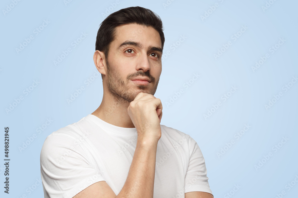 Attractive young man with dreamy cheerful expression thinking isolated on blue background