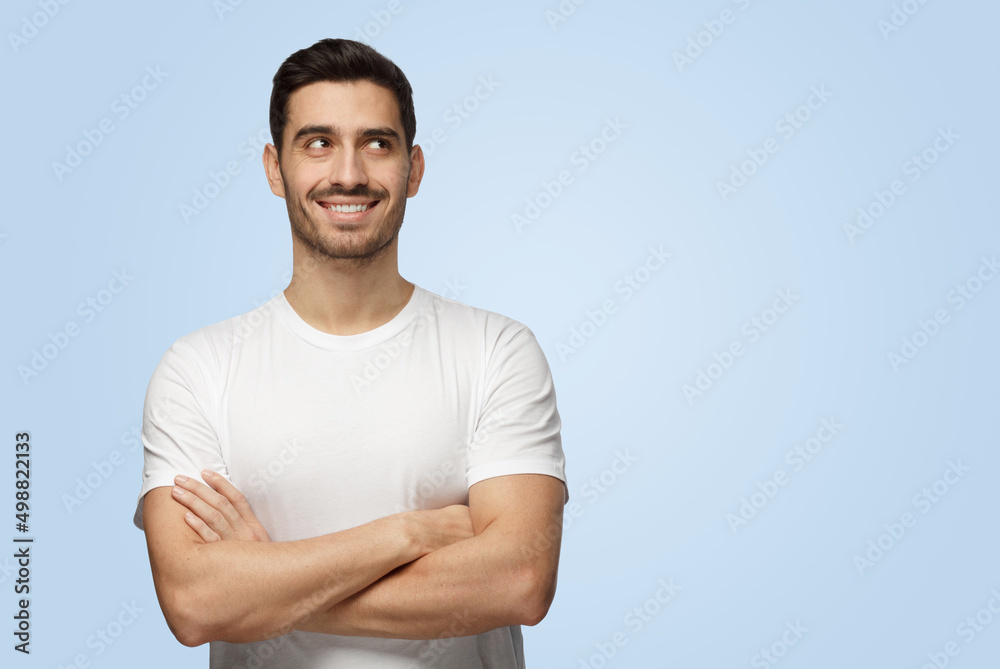 Attractive young optimistic dreamy man looks at camera standing with arms crossed Attractive young optimistic dreamy man looks at camera standing with arms crossed