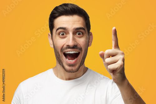 Smiling man wearing white tshirt pointing finger, having great innovative idea