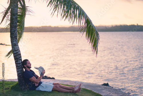 Tropical vacation. Young man resting under the palm tree.