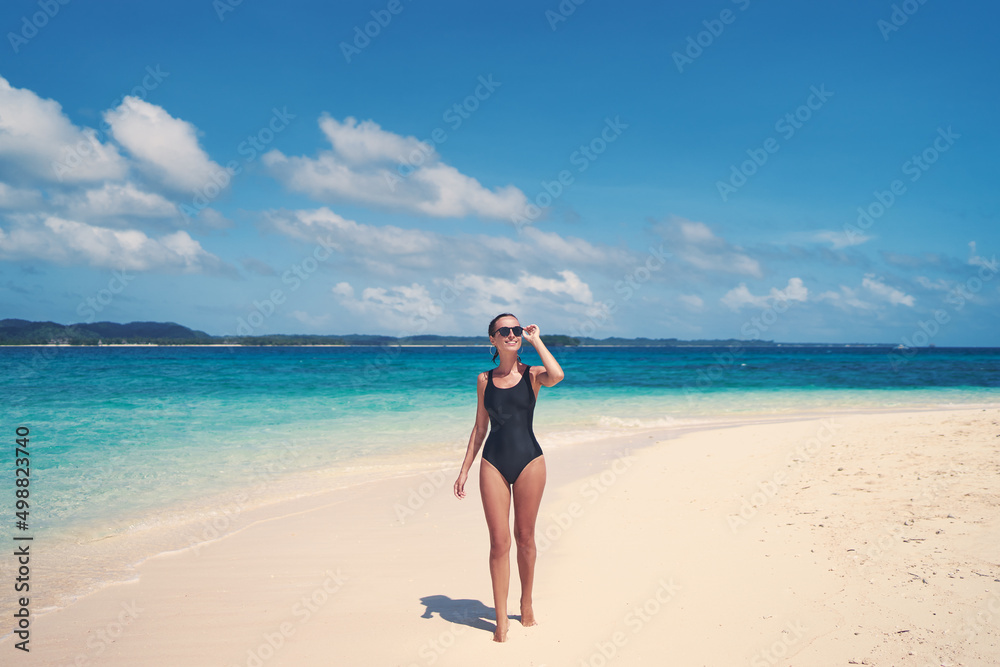 Vacation on the seashore. Back view of young woman walking on the beautiful tropical white sand beach.