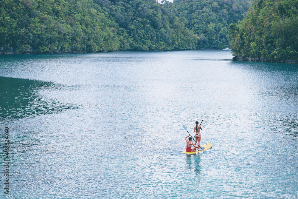 Summer holidays vacation travel. SUP Stand up paddle board. Young women sailing together on beautiful calm lagoon.