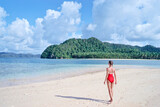Vacation on the seashore. Back view of young woman in red swimsuit walking away on the beautiful tropical white sand beach.