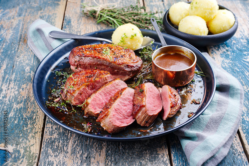 Traditionell gegrilltes Gourmet Entenbrust Filet mit Haut serviert mit Kartoffelknödel in Dunkelbier Sauce als close-up auf einem rustikalen Metall Tablett photo