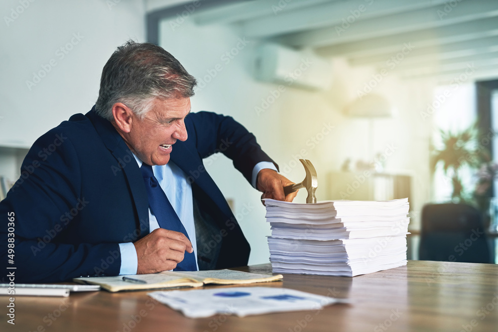 He has an alternative approach to paperwork. Shot of a frustrated businessman hitting a pile of paperwork with a hammer. He has an alternative approach to paperwork. Shot of a frustrated businessman hitting a pile of paperwork with a hammer.