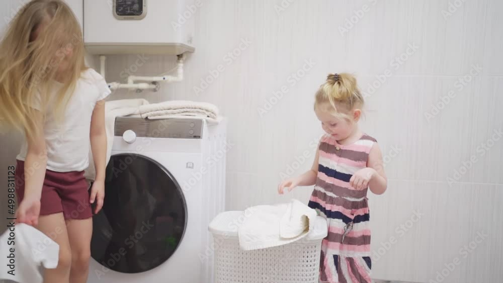 two cute and cheerful girls play with laundry in the laundry room. two cute and cheerful girls play with laundry in the laundry room.