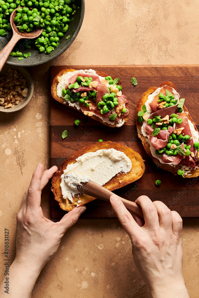 Hands spreading ricotta cheese on a crusty piece of bread next t Hands spreading ricotta cheese on a crusty piece of bread next t