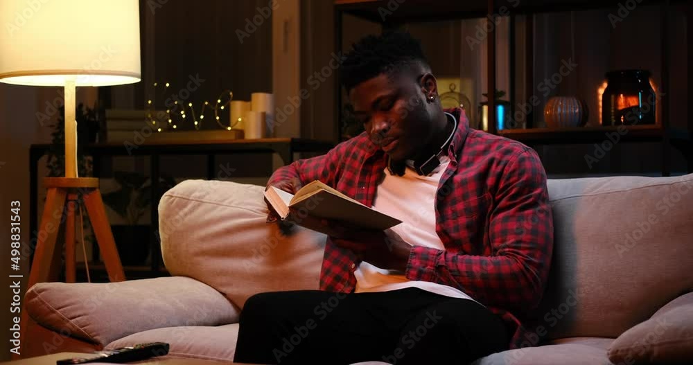 African American man reading a book late night at home