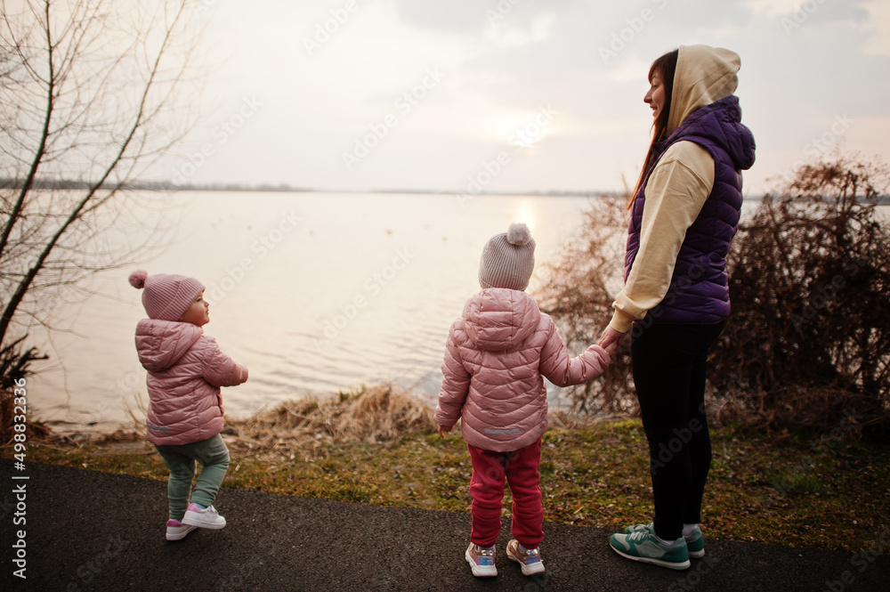 Fototapeta premium Mother with daughters walking on the path by the lake.