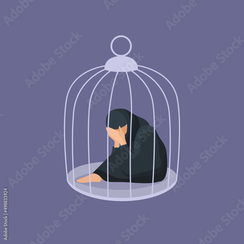 Muslim woman hugging her knees sitting inside of the cage. Concept of captivity, helplessness and depression