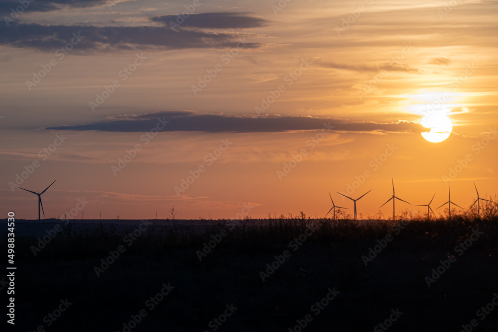 Wind turbines in field at sunset in yellow sun against backdrop of sunset sky in clouds. Beautiful landscape of sunset against background of wind turbines concept of environmentally friendly energy.