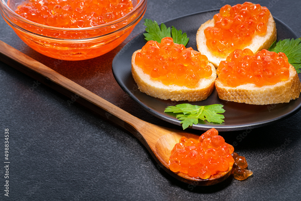 Red caviar in bowl of butter sandwich and in wooden spoon is close up of red caviar. Caviar on black background. Red caviar in bowl of butter sandwich and in wooden spoon is close up of red caviar. Caviar on black background.