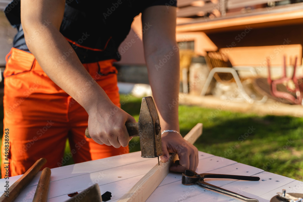 A man is hammering a nail in a plank on his workbench during the day A man is hammering a nail in a plank on his workbench during the day