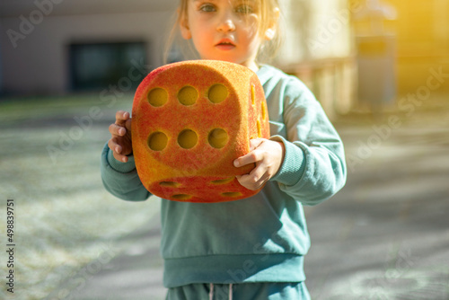 Child with a large red dice with the number six on the street during the day