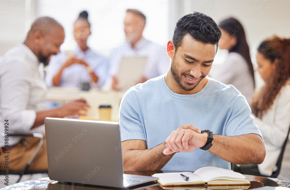 He knows how to manage his time productively and efficiently. Shot of a young businessman checking the time while working on a laptop in an office with his colleagues in the background. He knows how to manage his time productively and efficiently. Shot of a young businessman checking the time while working on a laptop in an office with his colleagues in the background.