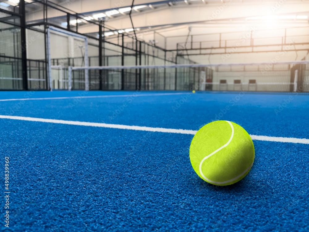 Draw of green ball over padel game placed on blue surface with white lines in spacious light court glowing light and net