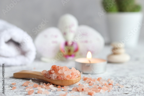 Beauty and spa concept. Pink himalayan salt close-up on a wooden spoon with candle, orchid flower and towel. Selective focus