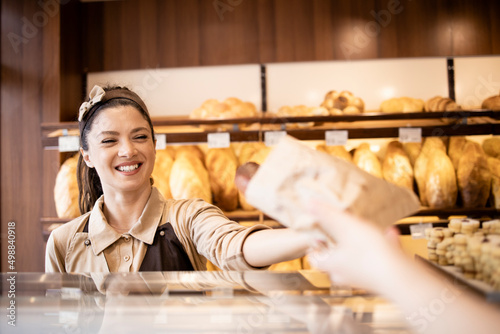 Beautiful woman working in bakery shop and selling fresh tasty pastry to the customer.