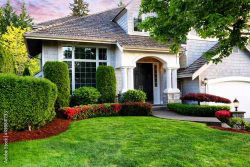 Photo Beautiful home exterior in evening with healthy green lawn and flowerbeds