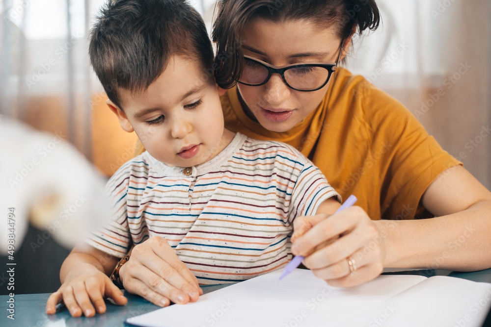 Mother teaching his son to write his name. Work and education from home for prevent coronavisrus COVID-19, self quarantine concept Mother teaching his son to write his name. Work and education from home for prevent coronavisrus COVID-19, self quarantine concept