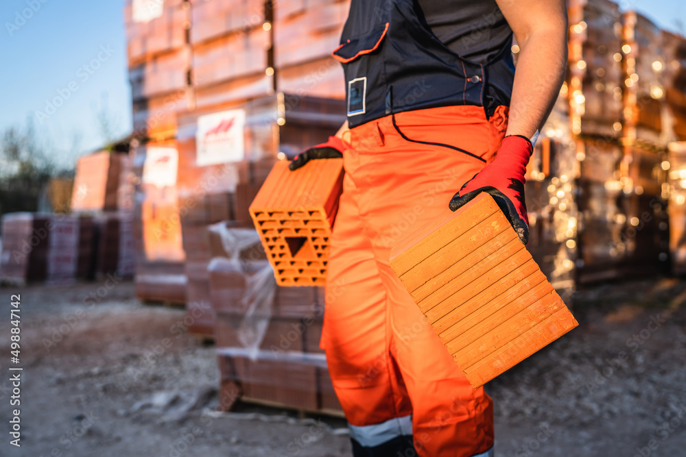 Close up on hands and midsection of unknown man construction worker taking orange hollow clay blocks ar warehouse or construction site in sunny summer day copy space Close up on hands and midsection of unknown man construction worker taking orange hollow clay blocks ar warehouse or construction site in sunny summer day copy space