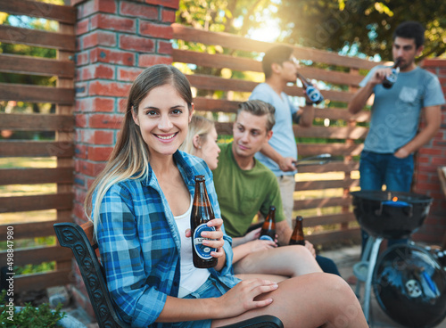 Another weekend, another chill sesh. Shot of a happy young woman enjoying a beer at a barbecue with her friends. photo