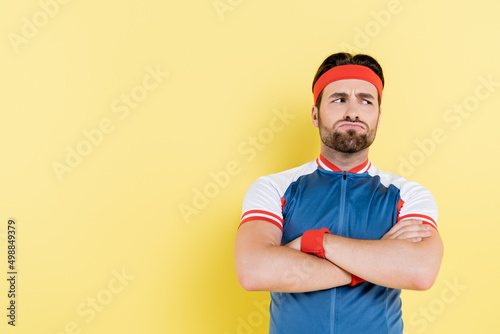 Pensive sportsman crossing arms isolated on yellow.