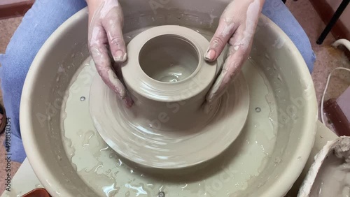 woman in a white shirt in a pottery workshop works with clay, on a potter's wheel. close-up hands in clay. craftsman at hand work.  photo